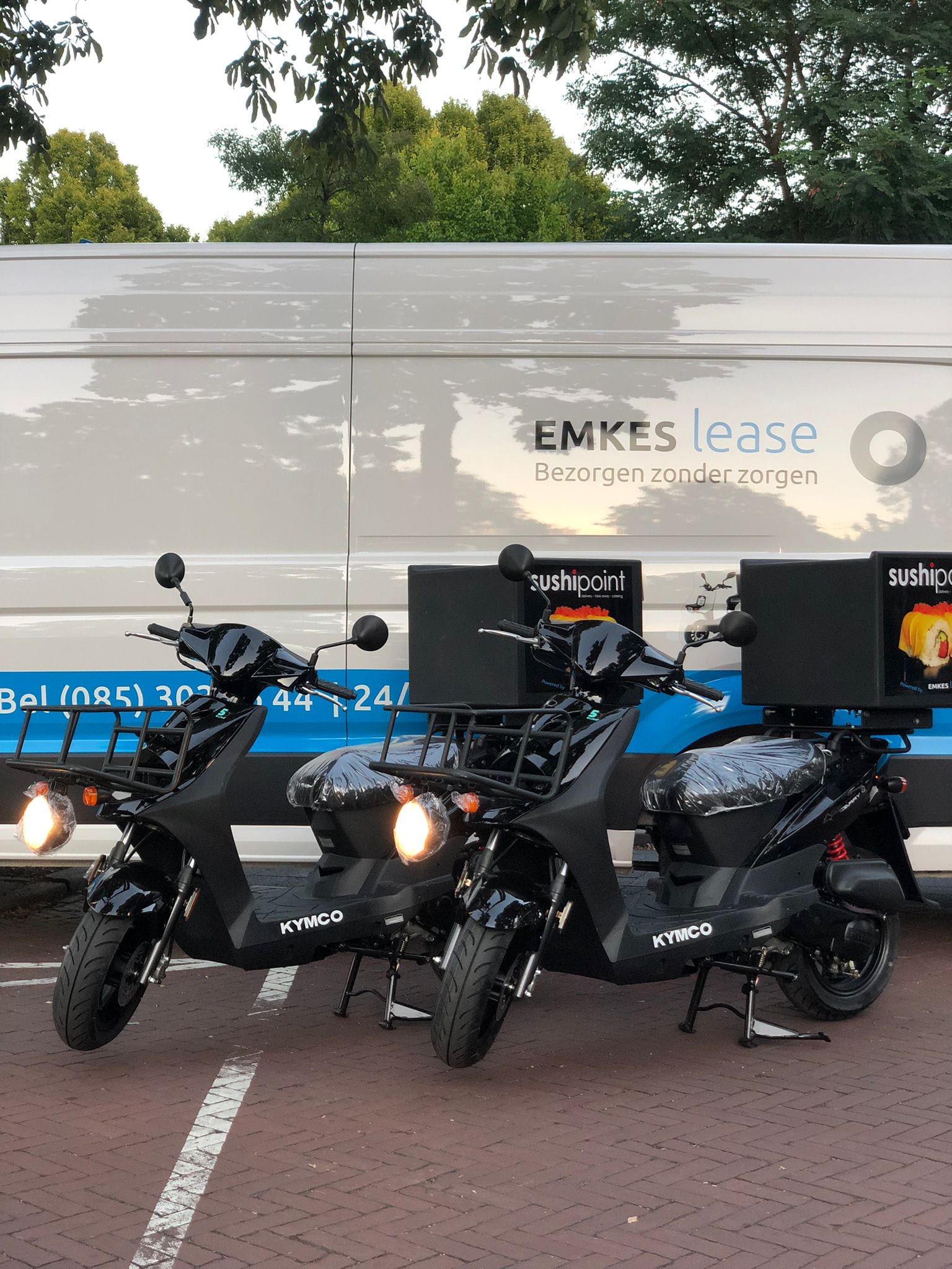 Twee zwarte bezorgscooters voor een bus van Emkes Lease