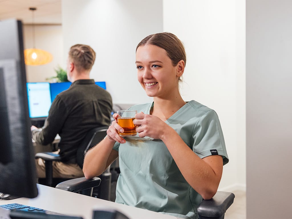 Lachende medewerker met een kop thee aan een bureau in de tandartspraktijk