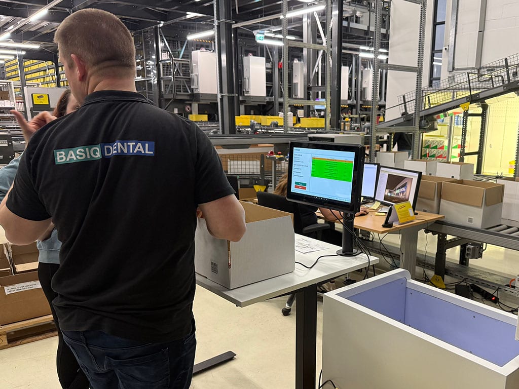 Medewerker van Basiq Dental controleert een doos bij een scanstation met scherm