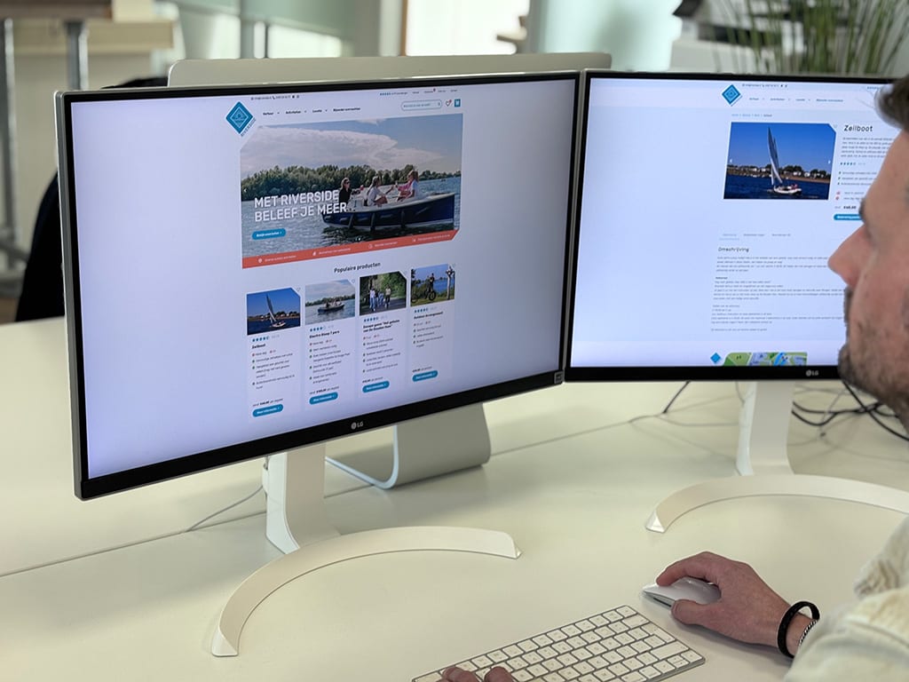 Medewerker werkt aan de webshop van Riverside Outdoor op twee schermen