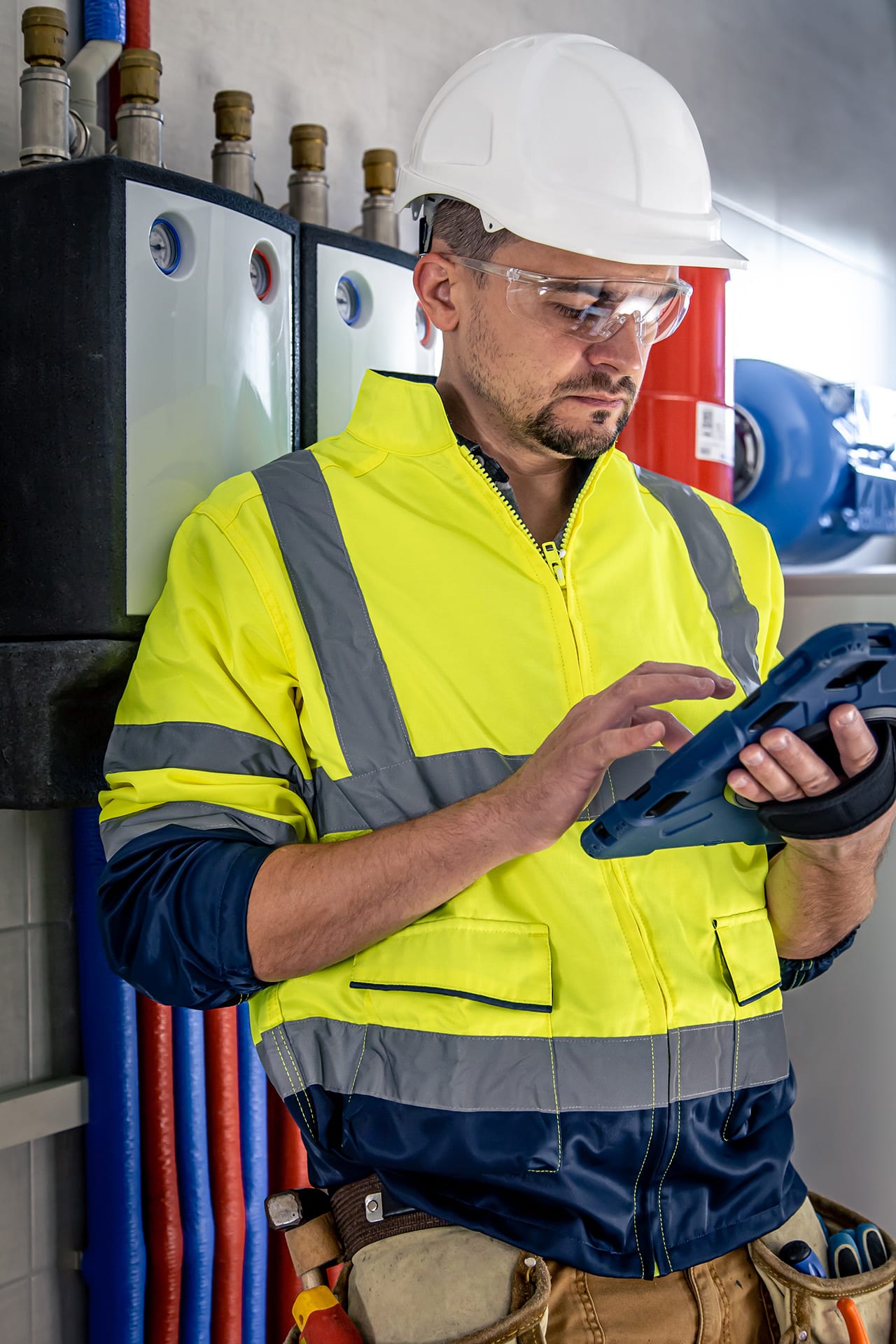 Monteur met helm en veiligheidshesje gebruikt een app op een robuuste tablet